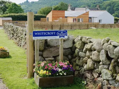 a sign in front of a stone wall with flowers at Myrtle Cottage - 28177 in Fairgirth