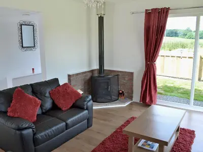 a living room with a black leather couch and a wood stove at Myrtle Cottage - 28177 in Fairgirth