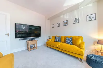 a living room with a yellow couch and a flat screen tv at Hazelgrove, Ratcliffe Place, Keswick in Keswick
