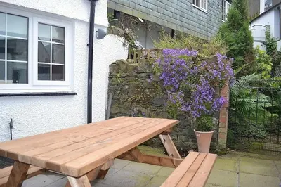 a wooden picnic table in front of a building with purple flowers at Oak Lodge in Keswick