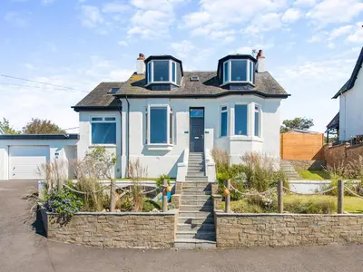 a white house with blue windows and a stone wall at Aird Cottage in Dunure