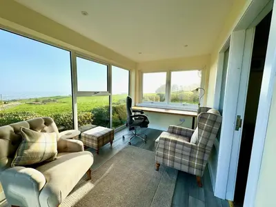 a living room with a couch and a chair and windows at High Auchenlarie Cottage in Gatehouse of Fleet