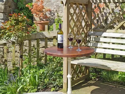 a bottle of wine on a table next to a bench at Earsdon Cottage in Ireby