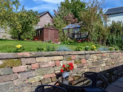 a stone retaining wall with a table with flowers on it at Southways Cottage in Cumwhinton