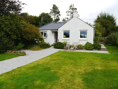 a white house with a lawn and chairs in a yard at Seabank Cottage in Rockcliffe