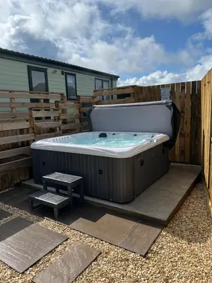 a hot tub sitting on a patio next to a fence at Maneight Luxury Lodge with hot tub in New Cumnock