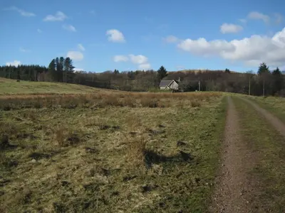 a dirt road in a field with a house in the distance at Rowantree Cottage in Gatehouse of Fleet
