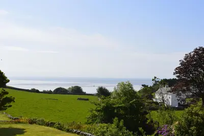 a field of green grass with a white house and the ocean at Portling View in Dalbeattie