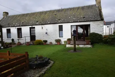 a white house with a yard with a clock in it at Ernambrie Cottage in Castle Douglas