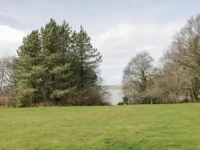 a field with trees and a lake in the background at Auchenvhin - Rockcliffe in Dalbeattie