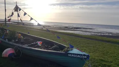 a boat sitting on the grass next to the beach at Roses Cottage cosy countryside home with open fire and mountain views near Scafell in Santon Bridge