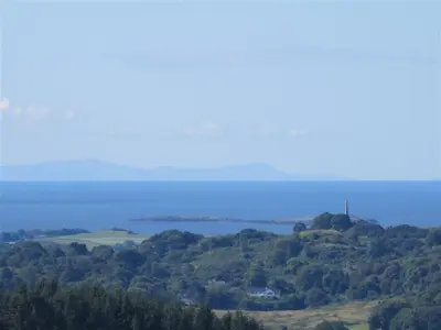 a view of a hill with trees and a body of water at Laghead Steading Cottage in Gatehouse of Fleet