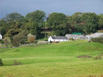 a green field with houses on top of a hill at Laghead Steading Cottage in Gatehouse of Fleet