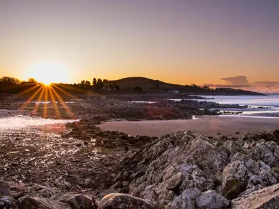 a sunset on a beach with rocks at Traditional Scottish Cottage in Beautiful Location - Pass the Keys in Rockcliffe