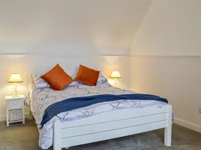a white bed with two orange pillows on it at Anchor Cottage in Portpatrick