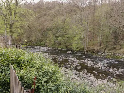 a river with rocks and trees and a fence at Pod No 5 in Keswick