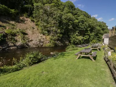 a picnic table on the grass next to a river at Riverside Cottage No 3 in Keswick