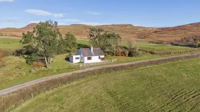 a white house in a field next to a road at Laghead Cottage in Gatehouse of Fleet