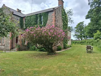 an old stone house with pink flowers in the yard at Threecrofts Farm in Dumfries