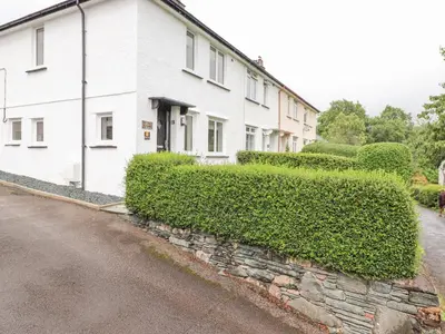 a white house with a hedge in front of a street at 1 Millbank in Keswick