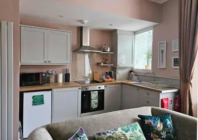 a kitchen with white cabinets and a couch in a room at The Ferns - Modern Apartment With Parking & Shared Garden in Darvel