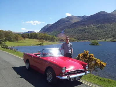 a man standing next to a red car on a road at Bluestones in Keswick