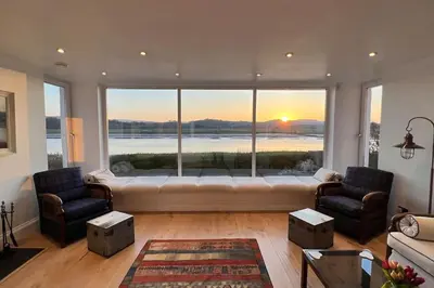 a living room with a large window with a couch and chairs at Shorepark - waterfront cottage with stunning views in Dumfries