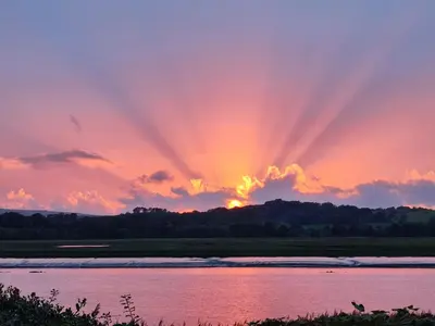 a sunset over a river with the sun setting in the sky at Shorepark - waterfront cottage with stunning views in Dumfries