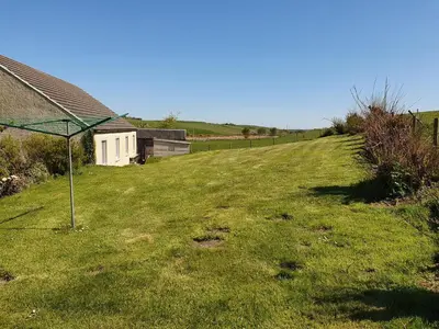 a grassy hill with a house and a field at Ash Cottage in Stranraer