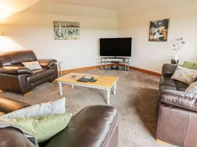 a living room with leather furniture and a flat screen tv at Middle Byre at Clauchan Holiday Cottages in Gatehouse of Fleet