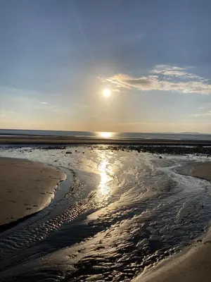 a beach with the sun shining on the water at Lake District Solway View 16 The Beeches Caravan Park in Gilcrux