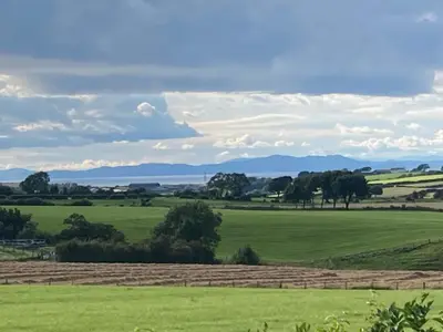 a green field with trees and mountains in the distance at Lake District Solway View 16 The Beeches Caravan Park in Gilcrux