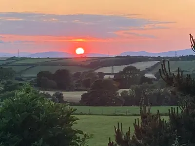 a sunset over a green field with trees at Lake District Solway View 16 The Beeches Caravan Park in Gilcrux