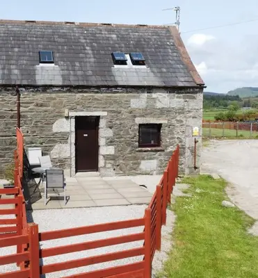 a stone house with a wooden fence in front of it at The Stable at Clauchan Holiday Cottages in Gatehouse of Fleet