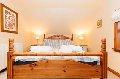 a bedroom with a large wooden bed with white pillows at The Stable at Clauchan Holiday Cottages in Gatehouse of Fleet