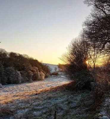 a snow covered field with a river with the sun setting at Willow Cottage, Gilchristland Organic Farm in Closeburn