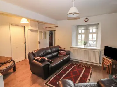 a living room with a leather couch and a piano at Kestrel Cottage in Keswick