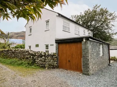 a white house with a stone wall and a wooden garage at Thwaite How in Keswick