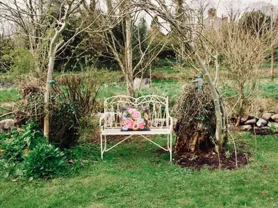 a white bench with a pillow sitting in the grass at Bridgend Cottage, Auchencairn, Castle Douglas in Auchencairn