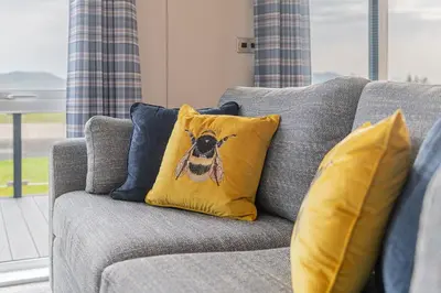 a couch with a pillow with a bee on it at Oak Tree Timber Holiday Lodge in Bassenthwaite