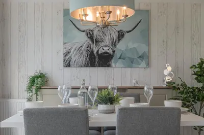 a dining room with a table with a cow picture on the wall at Birch Timber Holiday Lodge in Bassenthwaite