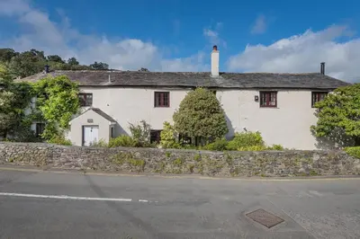 a white house with a stone wall next to a street at farmhouse braithwaite mews in Keswick