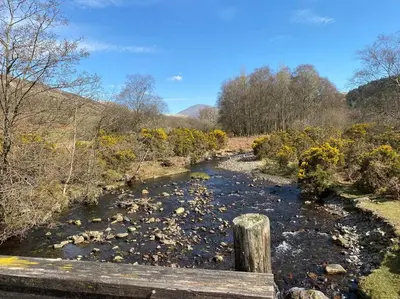 a bridge over a river with rocks and trees at Hillside Cottage Eskdale Green in Beckfoot