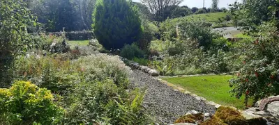 a garden with a gravel path and trees and bushes at Glenterry Farmhouse in Kirkcudbright