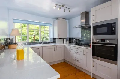 a kitchen with white cabinets and a large window at Bridge Cottage Keswick in Keswick