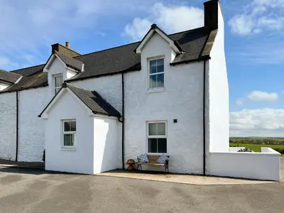 a white house with a bench in front of it at The Old Cheese Loft in Colfin