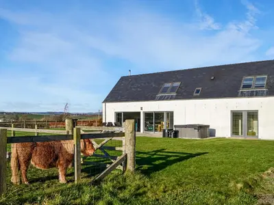 a horse standing behind a fence in front of a house at The Longhouse At Threave in Castle Douglas