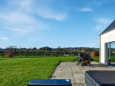 a patio with a table and chairs and a field at The Longhouse At Threave in Castle Douglas