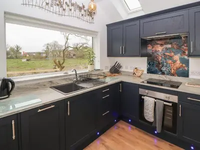 a kitchen with black cabinets and a large window at Cherry Croft in Wigton