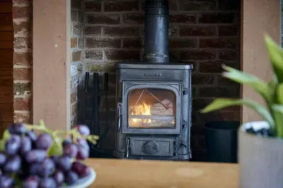 a stove in a brick fireplace with a bowl of grapes at Chiffchaff Lodge with Hot tub in Carlisle